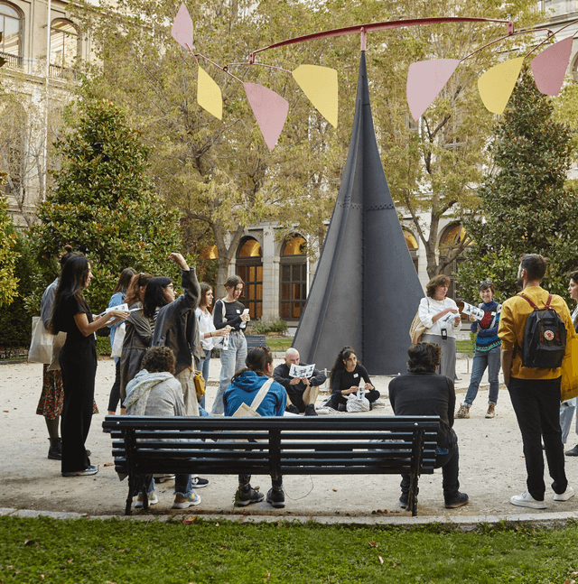 Un grupo de personas habla en círculo frente a la obra Carmen de Calder, en el jardín del Museo