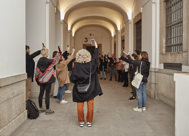 Un grupo de personas en un pasillo del Museo Reina Sofía elevan sus móviles por encima de sus cabezas y miran la pantalla.